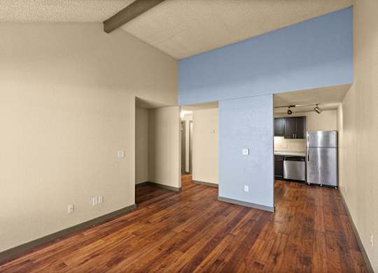 A room with wooden floors and a kitchen area in the background.