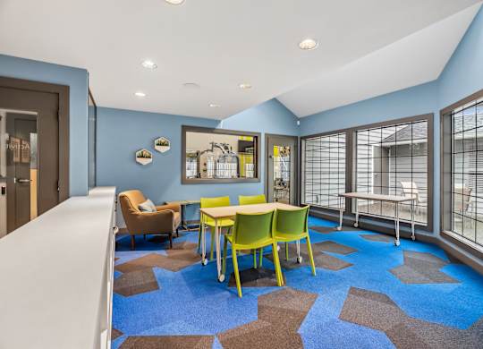A room with a blue carpet and a white table with yellow chairs.