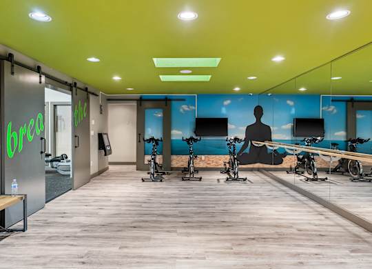 A gym with exercise bikes and a green logo on the wall.