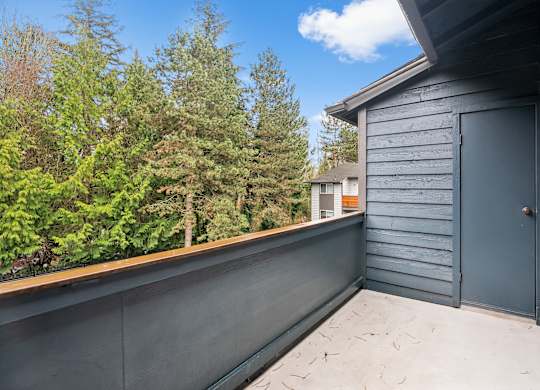 A grey deck with a door and a window overlooking a forest.