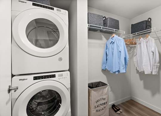 a laundry room with a washer and dryer and a closet with clothes hanging