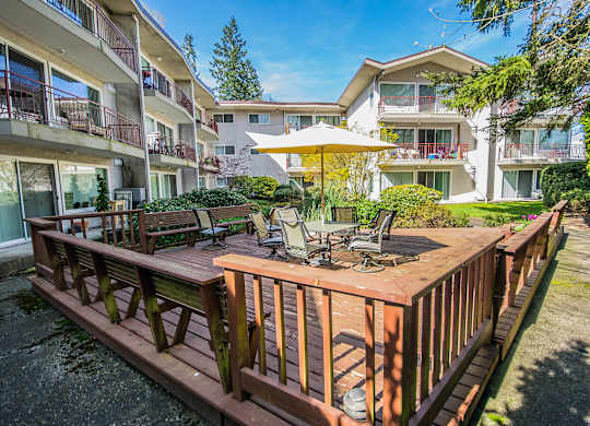 A wooden deck with chairs and a table is in the foreground of a sunny day.