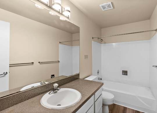 A bathroom with a sink, mirror, toilet and bathtub.