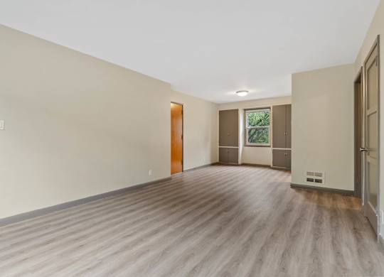 A room with wooden flooring and a window with a view of trees.