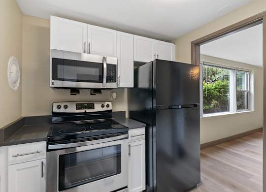 A black refrigerator stands next to a stove in a kitchen.