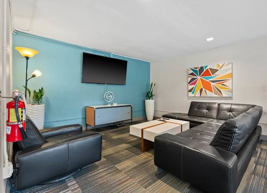 A black leather couch sits in a room with a blue wall and a television.