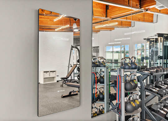 A gym with a mirror reflecting a workout area.