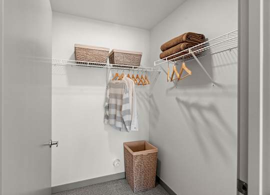 A white closet with a towel hanging on a rod and a basket on the floor.