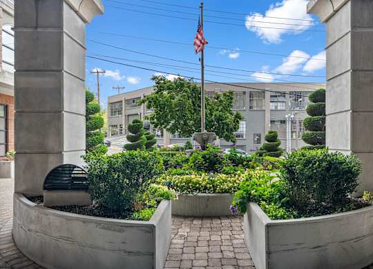 A garden with a flag on a pole is framed by two concrete pillars.