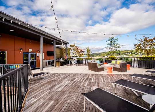 A wooden deck with chairs and tables is surrounded by a black railing. at The Platform, Kent, 98032