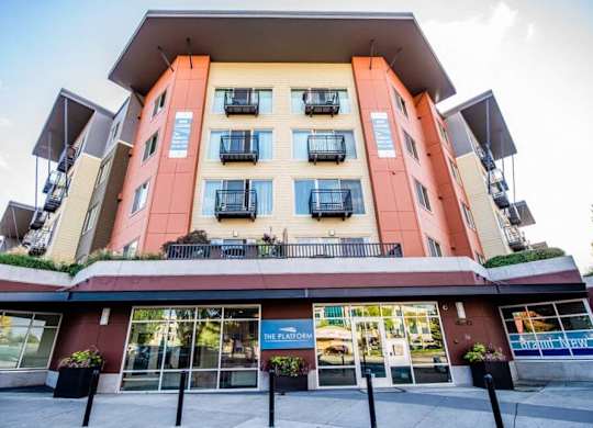 A multi-story building with a red and beige facade and balconies on the upper floors. at The Platform, Kent, 98032