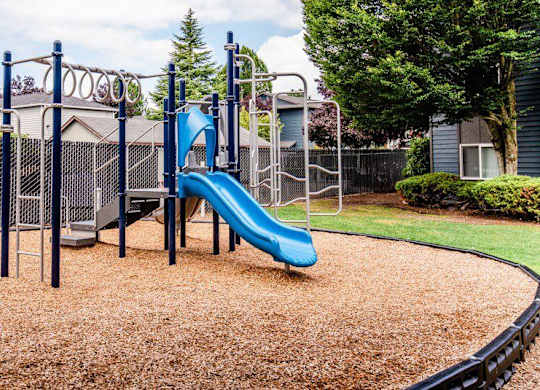 A playground with a blue slide and brown ground cover. at Vibe, Kent, WA
