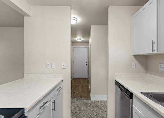 an empty kitchen with white countertops and white cabinets and a door to a hallway at Bellamy Park Apartments , Washington