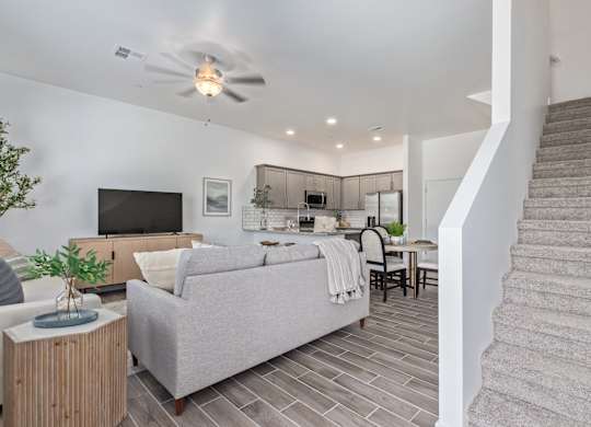 A living room with a grey couch, a television, a plant, and a staircase.