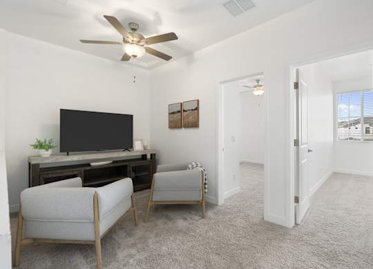 A living room with a television, two chairs, and a ceiling fan.