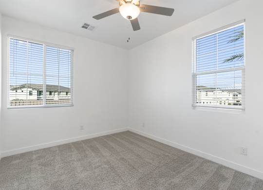 A room with a ceiling fan and two windows.