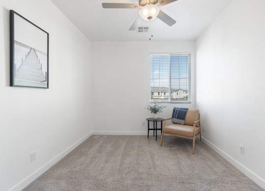 A room with a ceiling fan, a chair, and a small table with a plant on it.