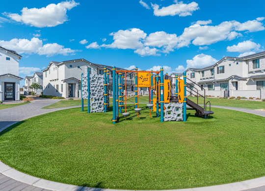 A playground with a slide and climbing wall in front of apartment buildings.