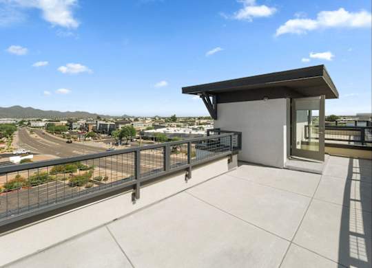 A balcony with a metal railing and a glass door overlooks a parking lot and distant buildings.
