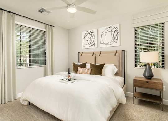 A bedroom with a large bed, a nightstand with a lamp, and two abstract art pieces on the wall.