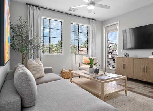 A living room with a grey couch, a wooden coffee table, and a flat screen TV mounted on the wall.