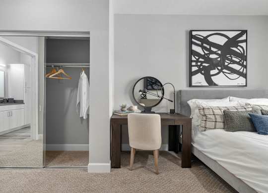 A bedroom with a bed, desk, chair, and a mirror.