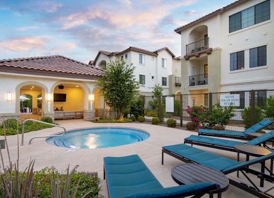 A pool surrounded by lounge chairs and a building in the background.