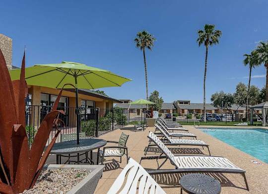 A poolside area with sun loungers and a green umbrella.