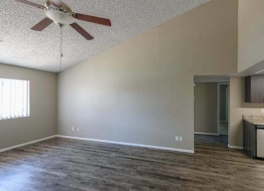 A room with a ceiling fan and a kitchen area in the background.