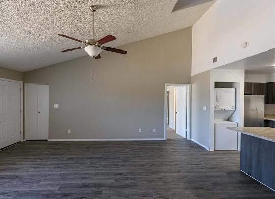 A room with a ceiling fan and a kitchen area in the background.
