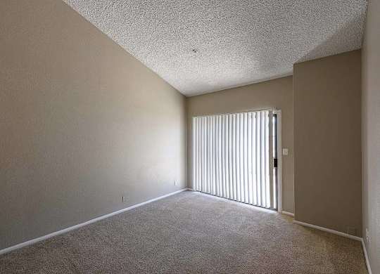 A room with a carpeted floor and a door with vertical blinds.