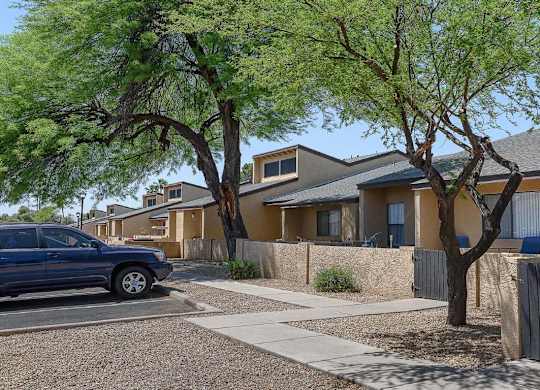 A blue car is parked on the street in front of a house with a tree in front of it.