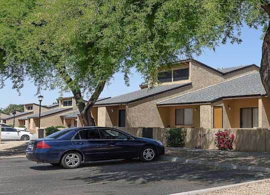 A blue car is parked in front of a house with a tree in front of it.