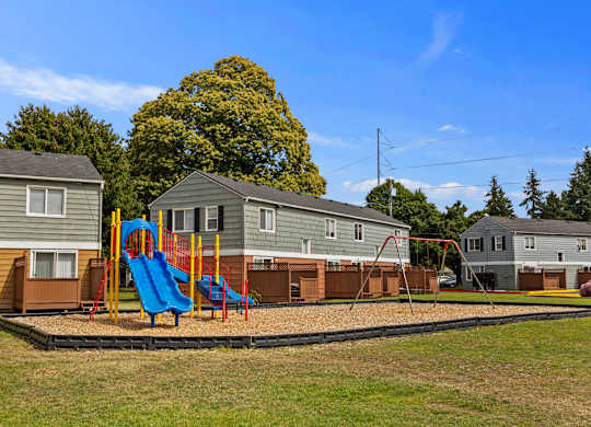 A playground with a blue slide and a red swing set in front of a row of houses.
