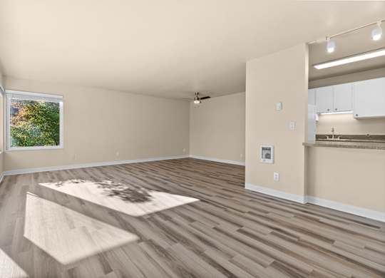 an empty living room with a kitchen and a window