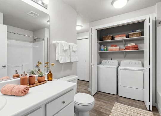 A white bathroom with a toilet, sink, and laundry room.