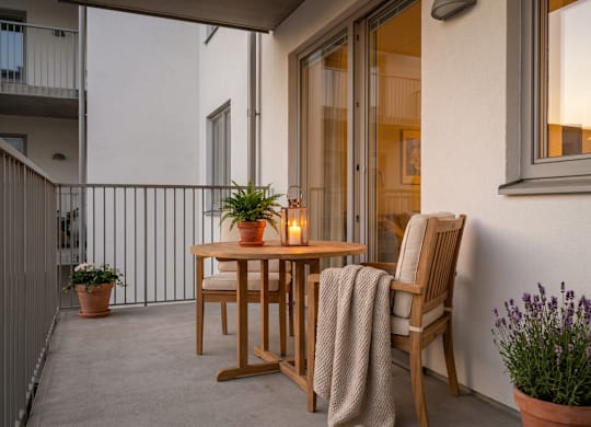 A wooden table with a blanket on a chair is on a balcony.