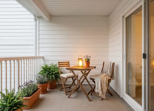 A small table with a blanket on a chair is on a balcony.