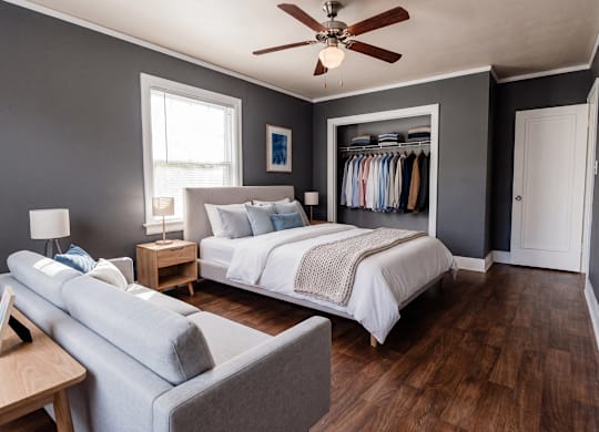 A bedroom with a bed, a couch, and a ceiling fan.