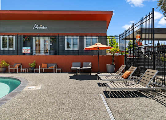 A pool area with a red building and lounge chairs.