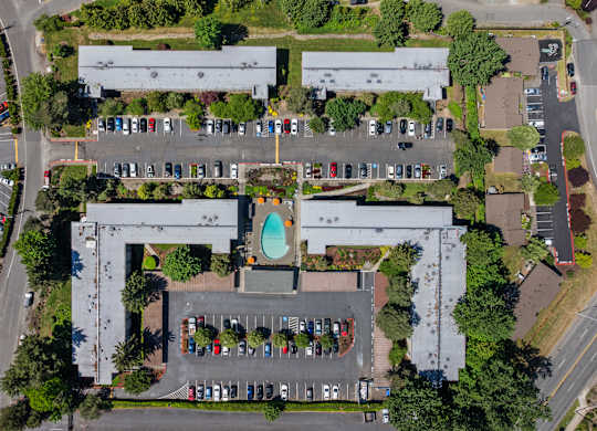 An aerial view of a parking lot with cars and a building with a pool in the middle.