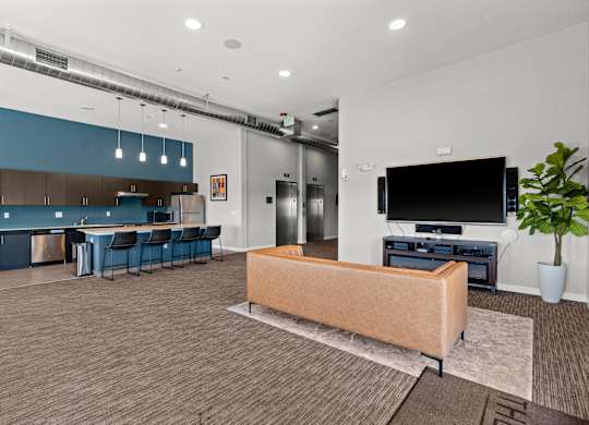 A modern living room with a sofa, a television, and a kitchen area in the background.