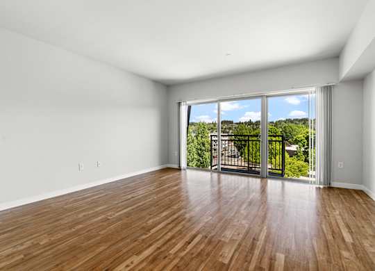 A room with wooden floors and a sliding glass door leading to a balcony.