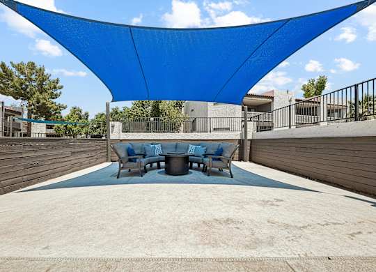 A blue shade structure is over a table and chairs.