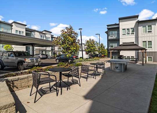 A patio area with chairs and a table in front of apartment buildings.