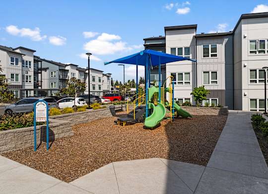 A playground with a blue canopy and a green slide in front of apartment buildings.