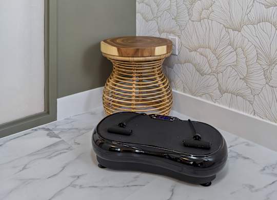 A black suitcase sits on a marble floor next to a round wooden stool.