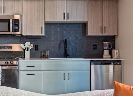 A modern kitchen with a white couch and a blue backsplash.