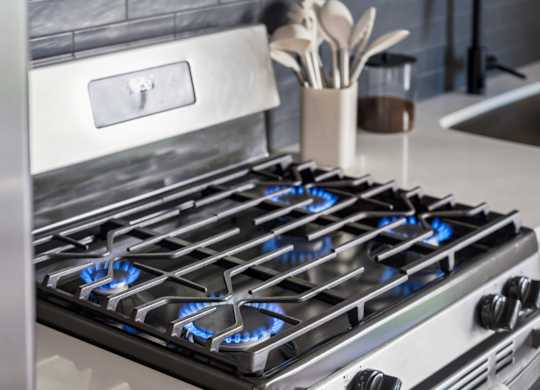 A modern gas stove with blue flames is in a kitchen.