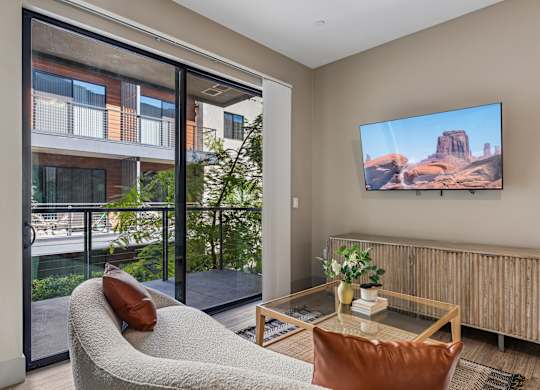 A living room with a couch, a table, a chair, and a television displaying a desert landscape.